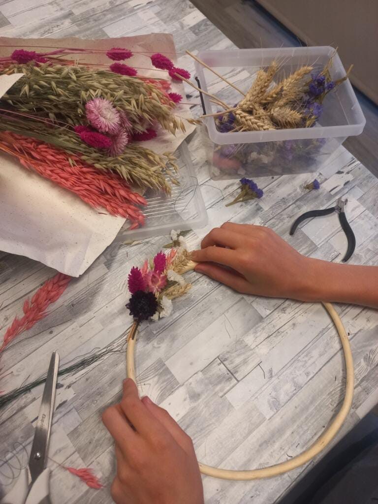Soline composant une couronne de fleurs séchées sur un cerceau dans son atelier